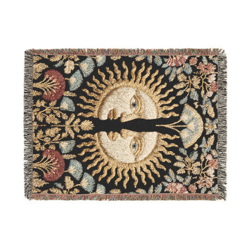 Jacquard-woven cotton blanket featuring twin celestial suns—two serene faces meeting at center—with radiant golden rays on a charcoal ground, bordered by folkloric botanicals and fan blossoms in sage, sky, and garnet. Crafted from 100% soft cotton yarn; the artwork is woven, not printed. Reversible with a color-negative back and finished with a protective 2-inch multicolor fringe. Sizes: 52×37, 50×60, 60×80 for wall, sofa, or queen-bed layering.